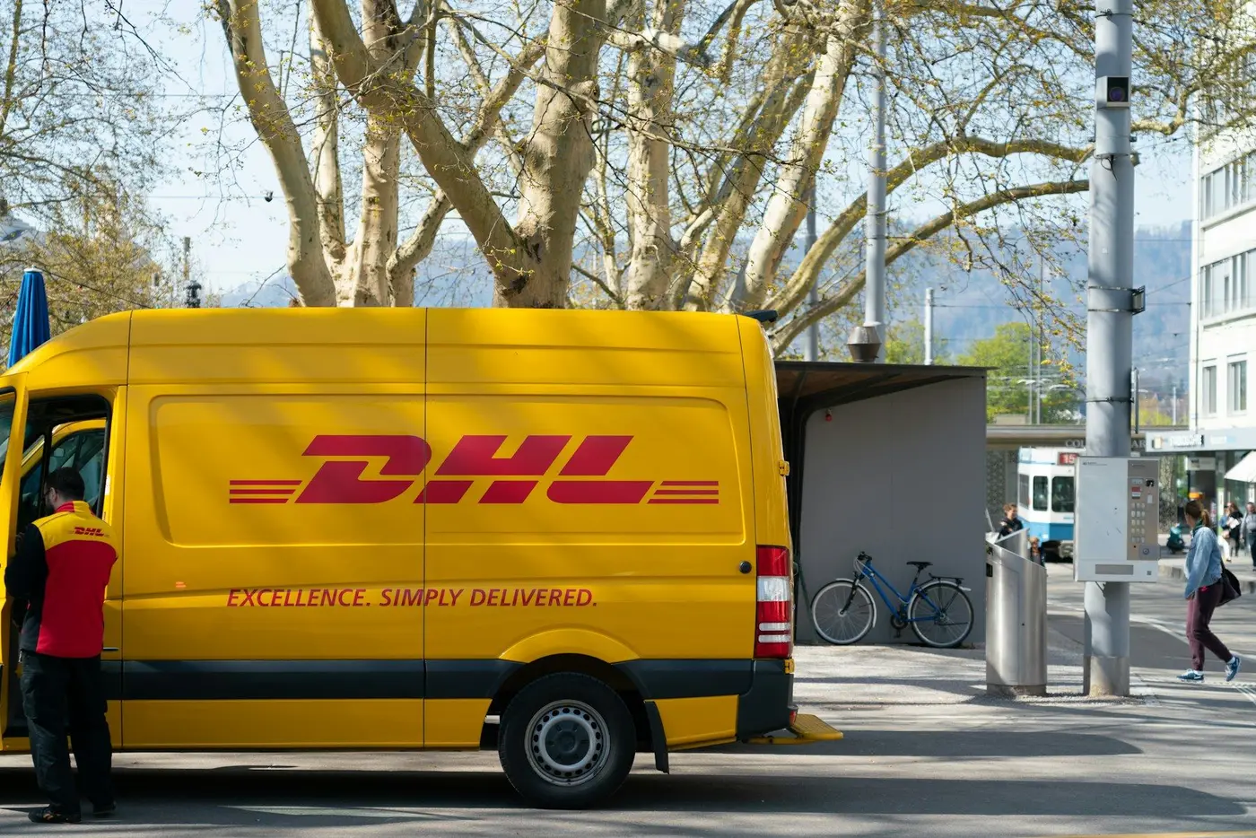 A DHL courier at the open door of a yellow DHL van